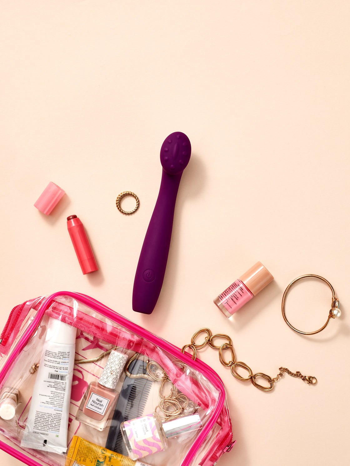 Blisshh Pleaser in deep violet placed with travel-sized cosmetics, lipstick, gold bracelet, and clear toiletry pouch.