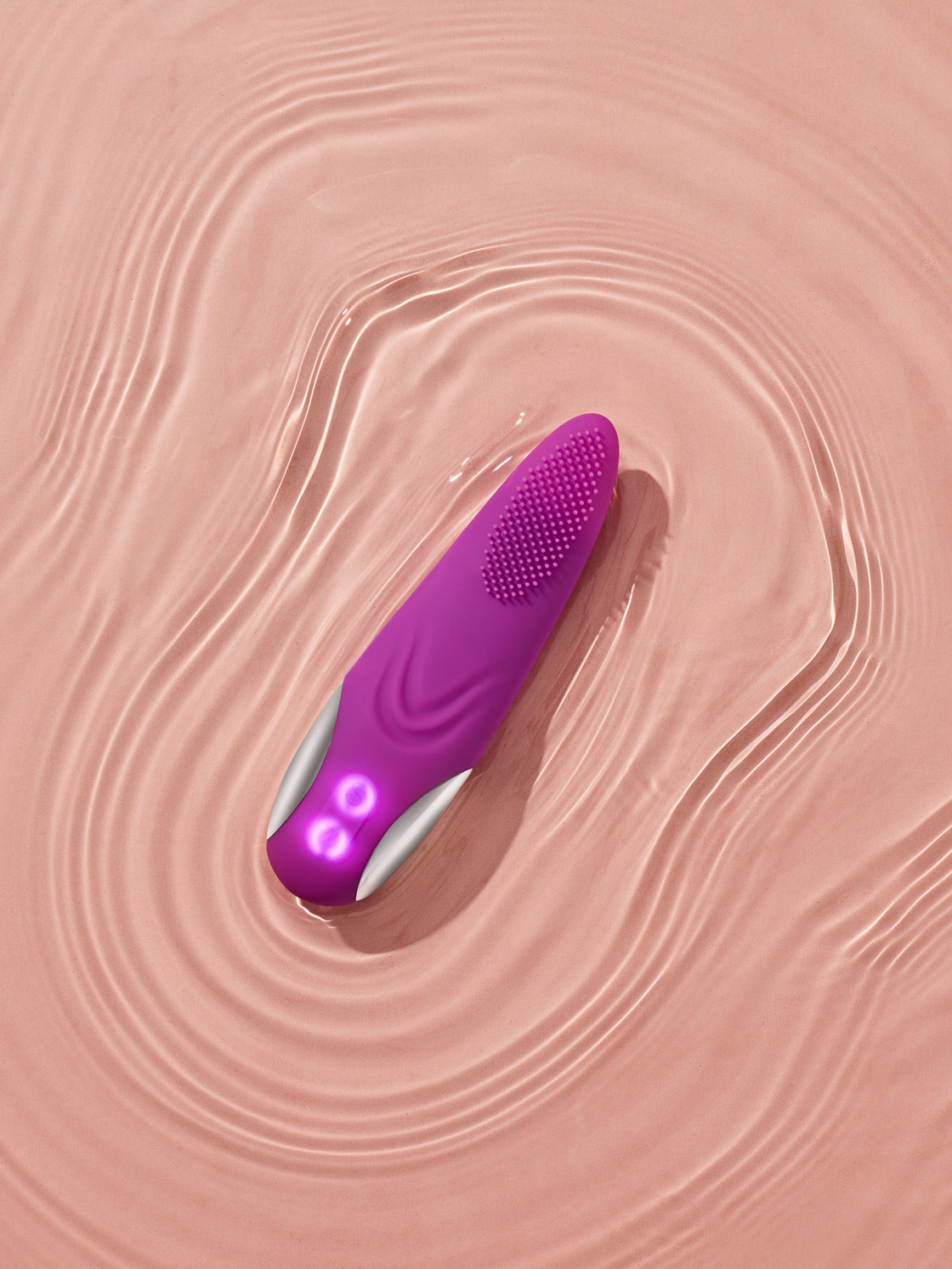 Blisshh Charmer device in magenta displayed on textured nude background, designed for facial and intimate care with soft silicone bristles.
