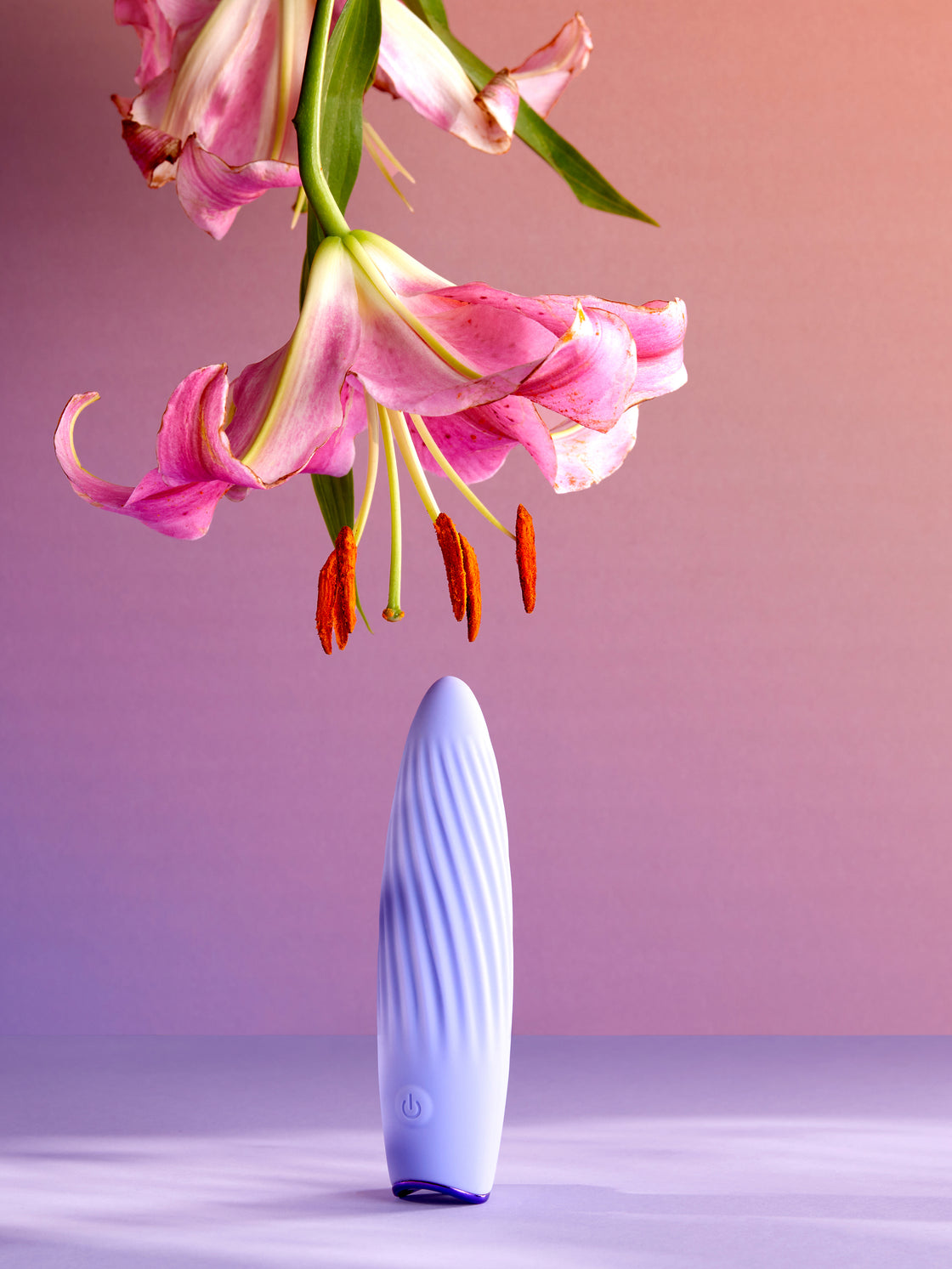 “Lavender Blisshh wellness device standing upright with a pink lily flower in a serene pastel setting.”